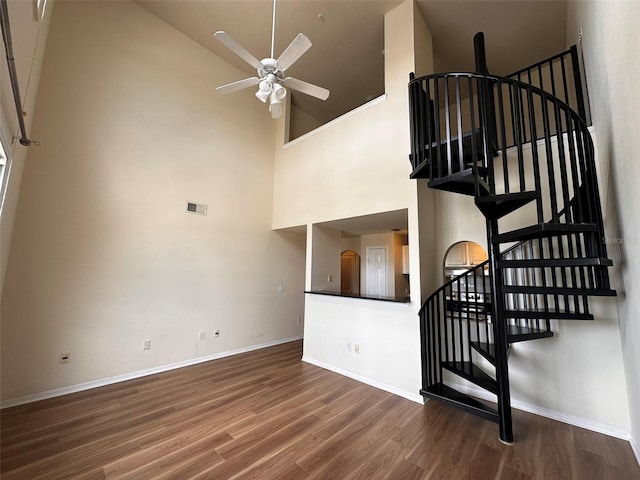 stairs featuring a high ceiling, wood-type flooring, and ceiling fan