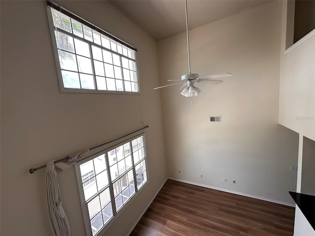 unfurnished living room with a high ceiling, ceiling fan, and dark wood-type flooring