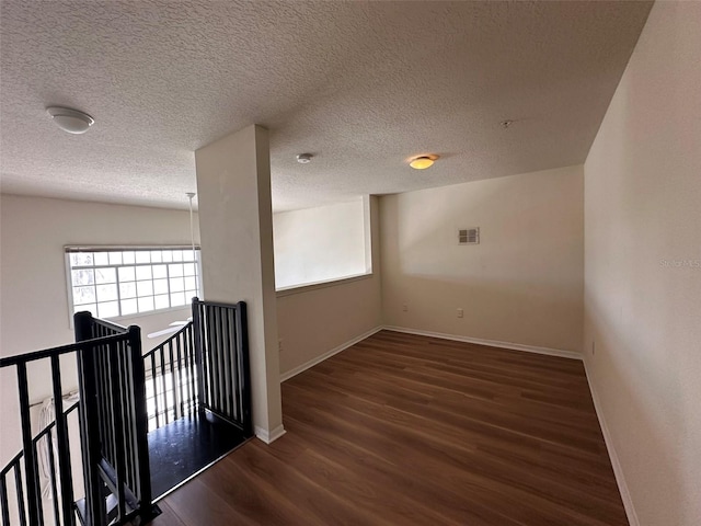 corridor with a textured ceiling and dark wood-type flooring