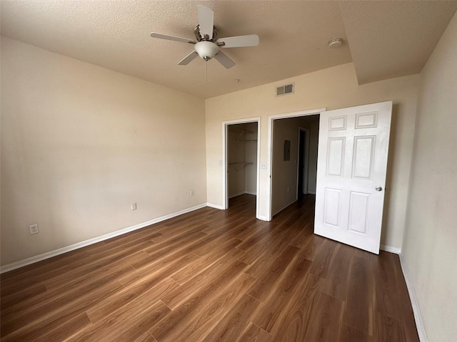 unfurnished bedroom featuring a spacious closet, a closet, ceiling fan, and dark hardwood / wood-style flooring