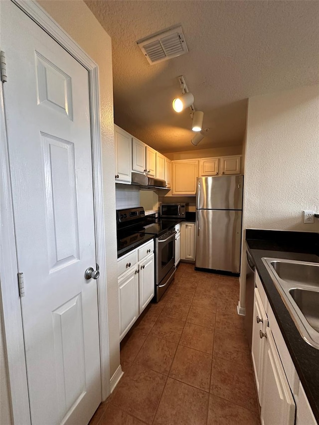 kitchen featuring dark tile patterned flooring, sink, a textured ceiling, white cabinetry, and appliances with stainless steel finishes