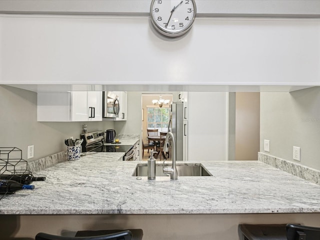 kitchen with kitchen peninsula, appliances with stainless steel finishes, sink, a notable chandelier, and white cabinetry