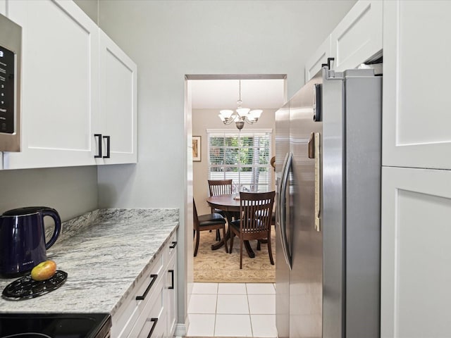 kitchen with light tile patterned floors, light stone counters, a notable chandelier, stainless steel fridge, and white cabinets