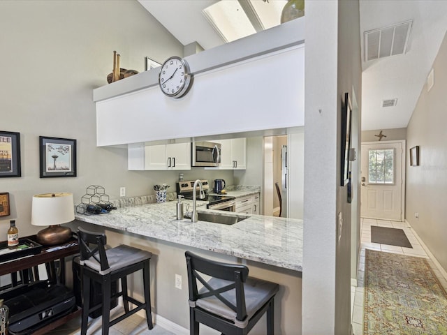 kitchen featuring white cabinets, sink, a kitchen bar, kitchen peninsula, and stainless steel appliances