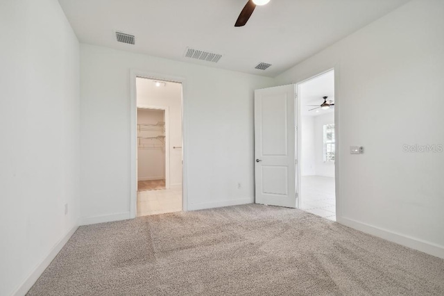 unfurnished bedroom featuring a spacious closet, a closet, ceiling fan, and light carpet