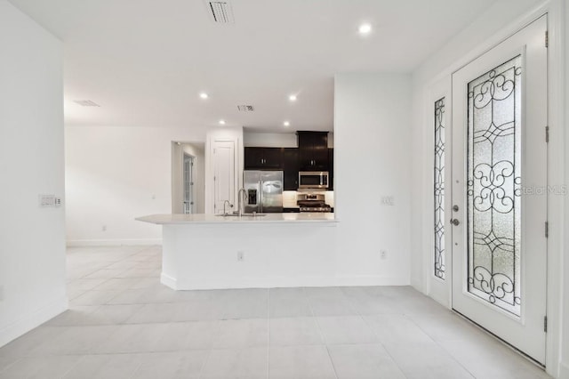 kitchen with kitchen peninsula, dark brown cabinets, light tile patterned floors, and stainless steel appliances