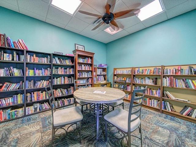 sitting room with ceiling fan, carpet floors, and a drop ceiling