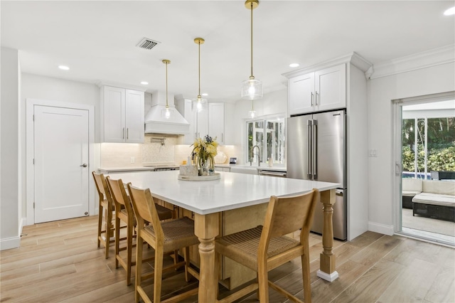 kitchen featuring white cabinetry, stainless steel appliances, hanging light fixtures, and premium range hood