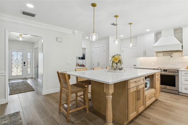 kitchen featuring white cabinetry, custom exhaust hood, hanging light fixtures, a center island, and stainless steel appliances