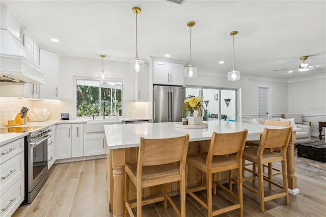 kitchen with white cabinetry, hanging light fixtures, stainless steel appliances, and a kitchen bar