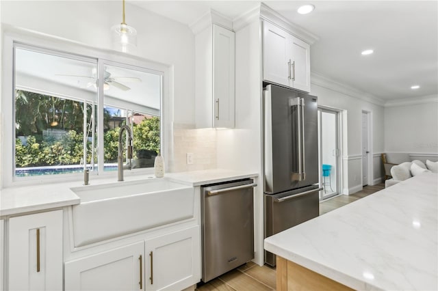 kitchen featuring pendant lighting, sink, appliances with stainless steel finishes, light stone countertops, and white cabinets