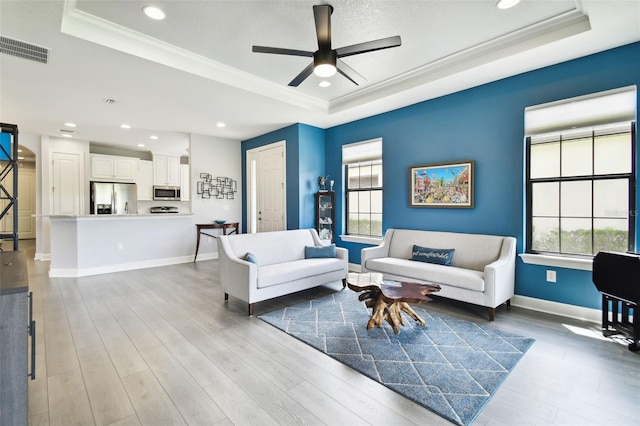 living room featuring ornamental molding, a tray ceiling, ceiling fan, and a wealth of natural light