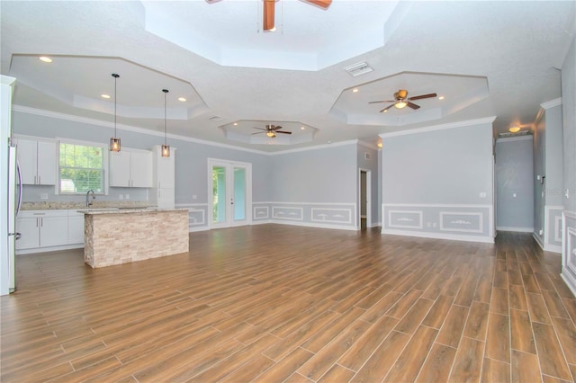 unfurnished living room with a tray ceiling, dark wood-type flooring, ornamental molding, and ceiling fan