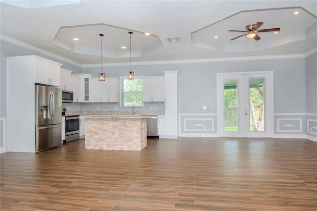 kitchen featuring stainless steel appliances, a center island, white cabinets, decorative light fixtures, and a raised ceiling