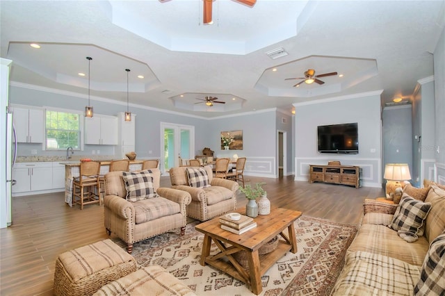 living room with a raised ceiling, crown molding, hardwood / wood-style flooring, and ceiling fan