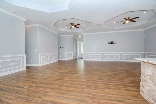 unfurnished living room with ceiling fan, ornamental molding, a raised ceiling, and wood finished floors