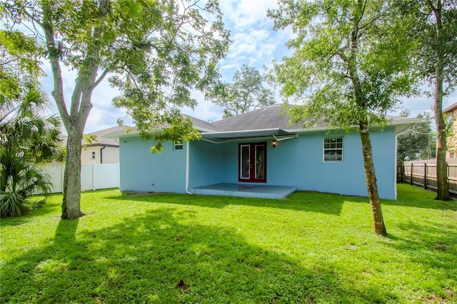 rear view of house with french doors, a fenced backyard, a yard, and stucco siding