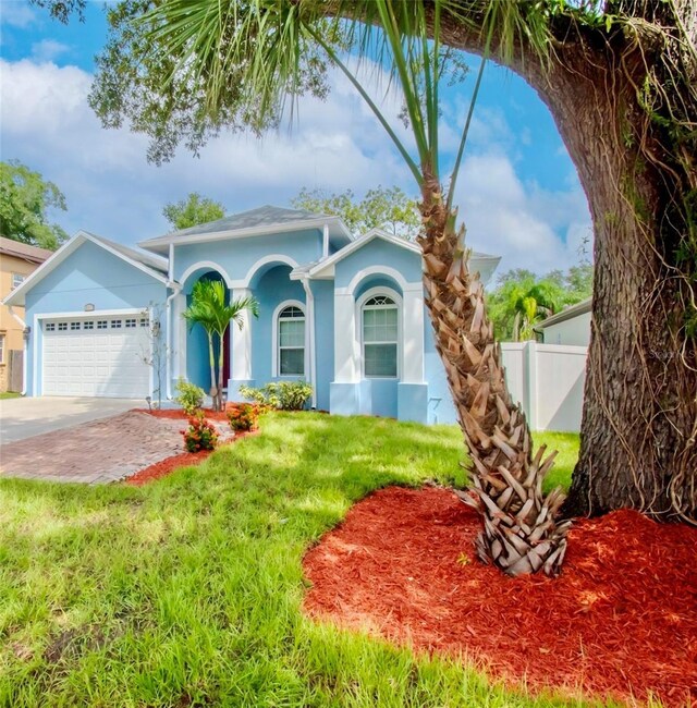 view of front facade with stucco siding, a front yard, fence, a garage, and driveway