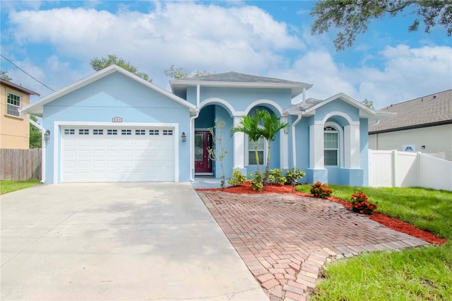 ranch-style house featuring an attached garage, fence, concrete driveway, and stucco siding