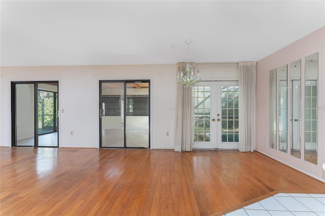 spare room with an inviting chandelier, light wood-type flooring, and french doors