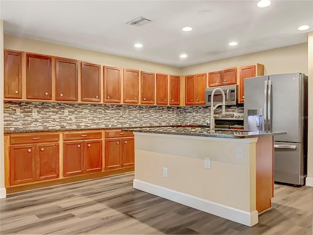 kitchen featuring light hardwood / wood-style flooring, stainless steel appliances, tasteful backsplash, and a kitchen island with sink