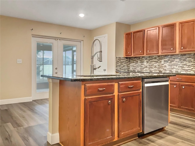 kitchen featuring light wood-type flooring, tasteful backsplash, dishwasher, sink, and a center island with sink