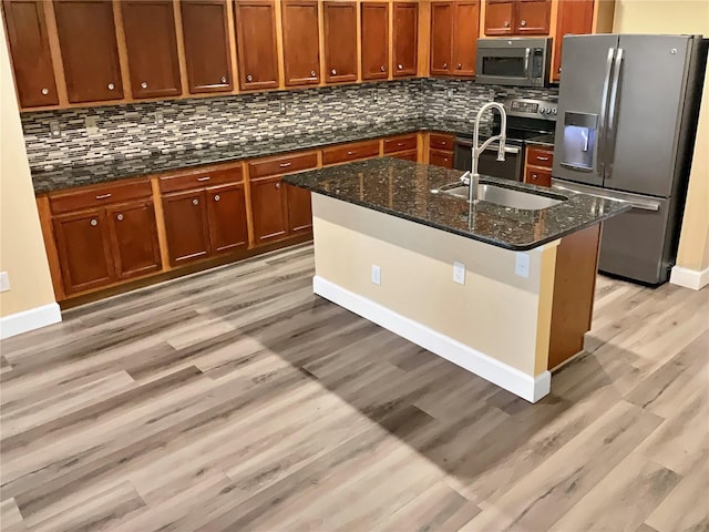 kitchen with appliances with stainless steel finishes, light hardwood / wood-style floors, and dark stone counters