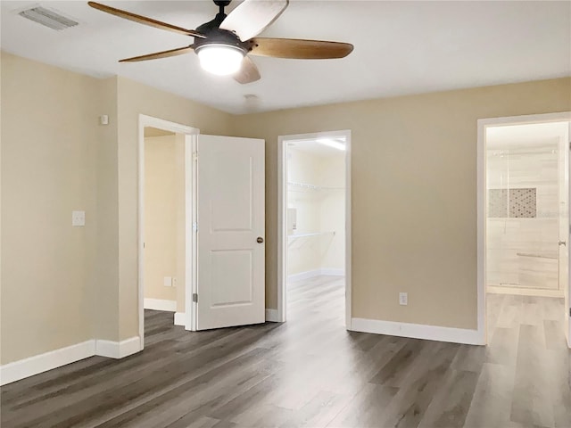 unfurnished bedroom featuring dark wood-type flooring, a walk in closet, ensuite bathroom, and ceiling fan