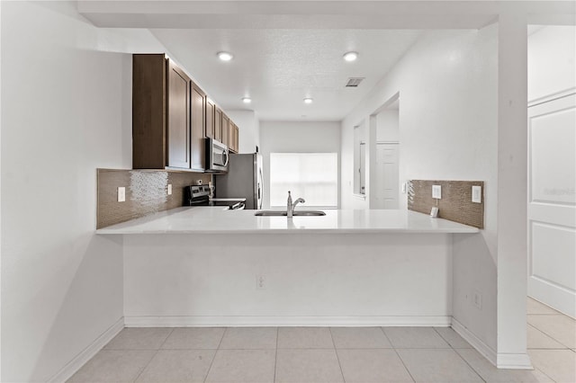 kitchen featuring appliances with stainless steel finishes, decorative backsplash, kitchen peninsula, dark brown cabinets, and sink