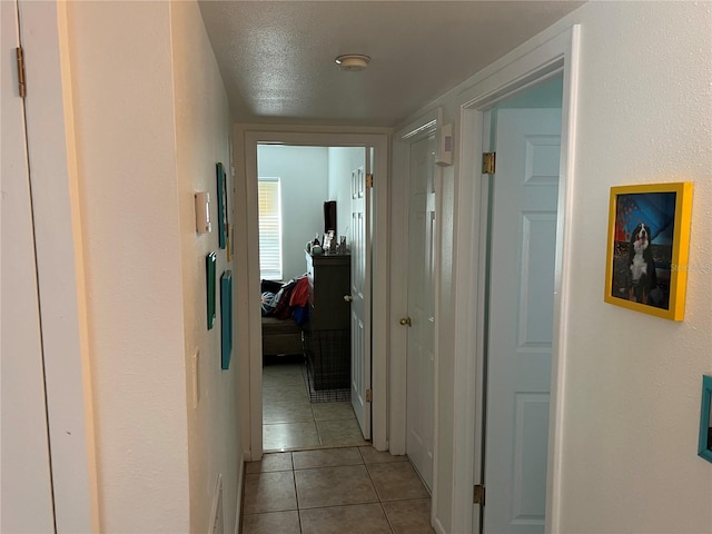 hallway with a textured ceiling and light tile patterned floors