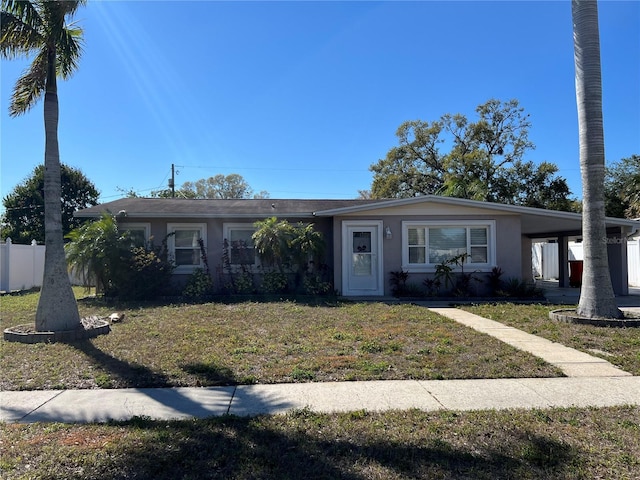 view of front facade with fence, a front lawn, an attached carport, and stucco siding