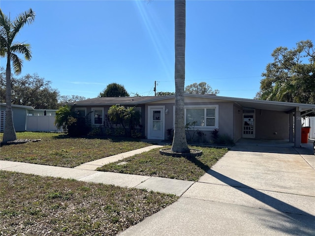 view of front facade with stucco siding, concrete driveway, fence, a carport, and a front lawn