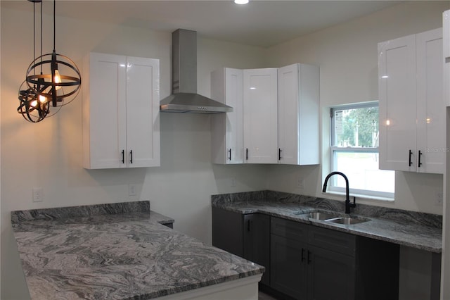 kitchen featuring decorative light fixtures, wall chimney exhaust hood, sink, and white cabinets