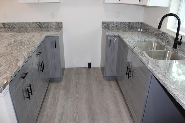 kitchen featuring light stone counters, light wood-type flooring, sink, and gray cabinetry