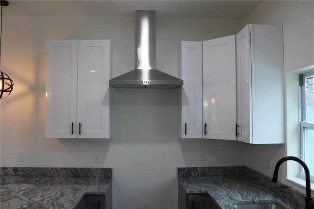 kitchen with wall chimney exhaust hood, dark stone countertops, sink, and white cabinets