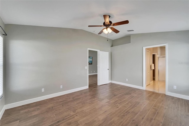 interior space with ceiling fan, hardwood / wood-style floors, a walk in closet, ensuite bathroom, and vaulted ceiling