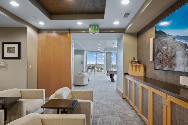 hallway with a barn door, a raised ceiling, carpet flooring, and expansive windows