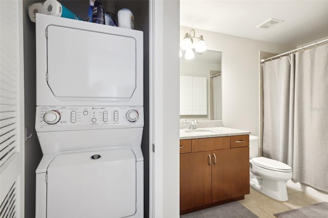 washroom with stacked washer / drying machine, sink, light tile patterned floors, and a chandelier