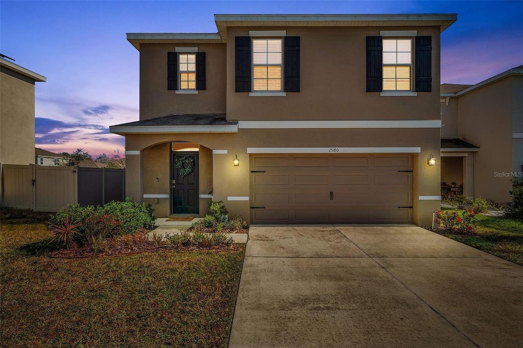 traditional home featuring concrete driveway, fence, an attached garage, and stucco siding