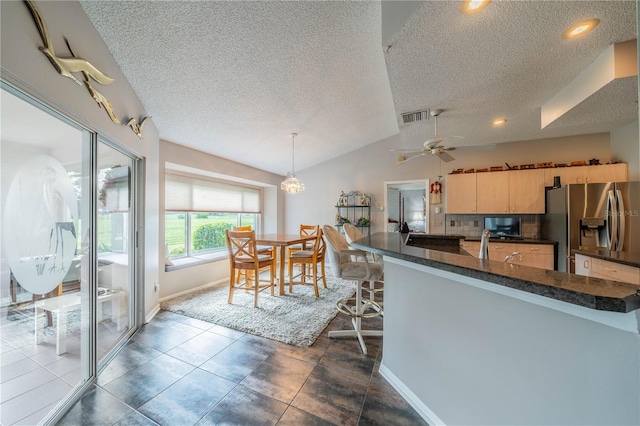 kitchen featuring a textured ceiling, stainless steel refrigerator with ice dispenser, decorative light fixtures, vaulted ceiling, and light brown cabinets