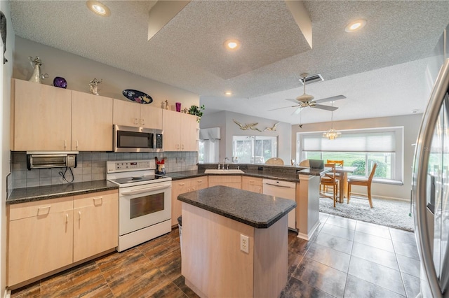 kitchen with a textured ceiling, appliances with stainless steel finishes, a kitchen island, light brown cabinetry, and kitchen peninsula