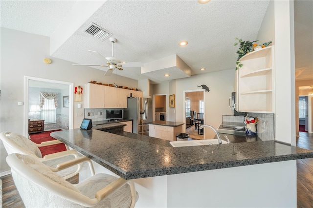 kitchen featuring a textured ceiling, stainless steel refrigerator with ice dispenser, sink, kitchen peninsula, and a breakfast bar area