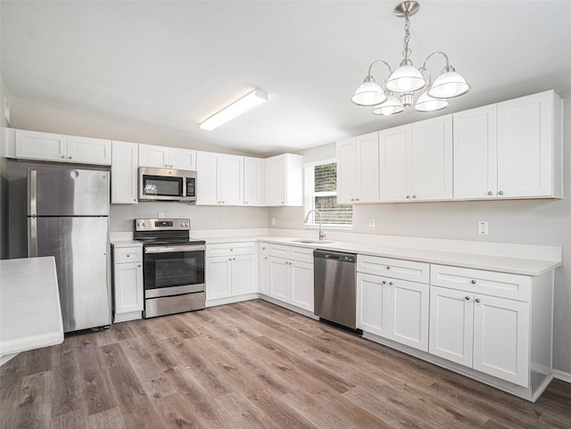 kitchen featuring pendant lighting, white cabinetry, stainless steel appliances, an inviting chandelier, and light wood-type flooring