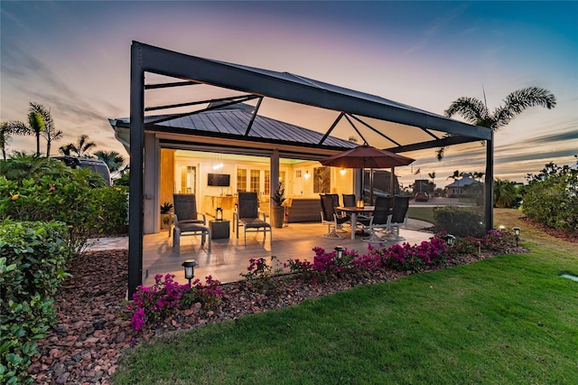 back house at dusk with a lawn and a patio area