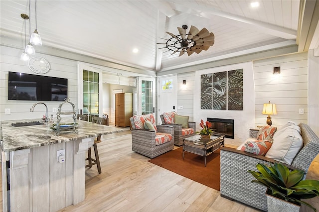 living room with ceiling fan, beam ceiling, sink, a fireplace, and light wood-type flooring