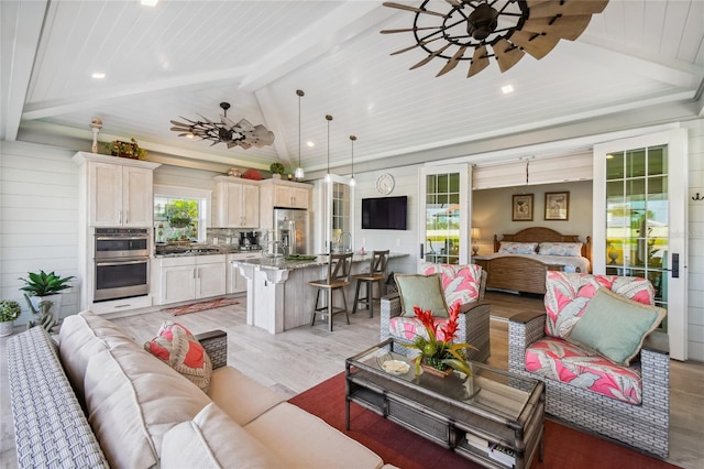 living room featuring lofted ceiling with beams, wooden walls, light hardwood / wood-style floors, and ceiling fan