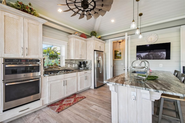 kitchen with dark stone counters, a breakfast bar area, light hardwood / wood-style flooring, appliances with stainless steel finishes, and decorative light fixtures