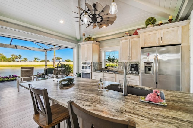 kitchen featuring light hardwood / wood-style floors, lofted ceiling with beams, tasteful backsplash, light brown cabinets, and stainless steel appliances