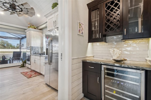 kitchen with appliances with stainless steel finishes, white cabinetry, wine cooler, tasteful backsplash, and light wood-type flooring