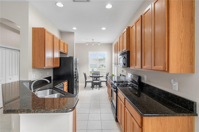 kitchen featuring rail lighting, dark stone countertops, light tile patterned floors, black appliances, and sink